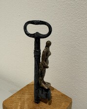 Mixed Media Objekte, Kunst, Eisenschlüssel mit Keramikfigur auf Holzsockel. Die kleinen gebrannten Figuren schimmern bronzefarbig.